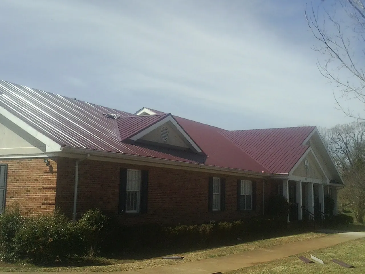 Red metal roof with gabled entries on a long brick building, from a Hail Damage Roof Repair job in Wallsburg