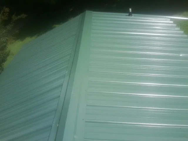 New green metal panels meeting at the ridge of a roof — Flat Roof Repair work by our crew in Wallsburg