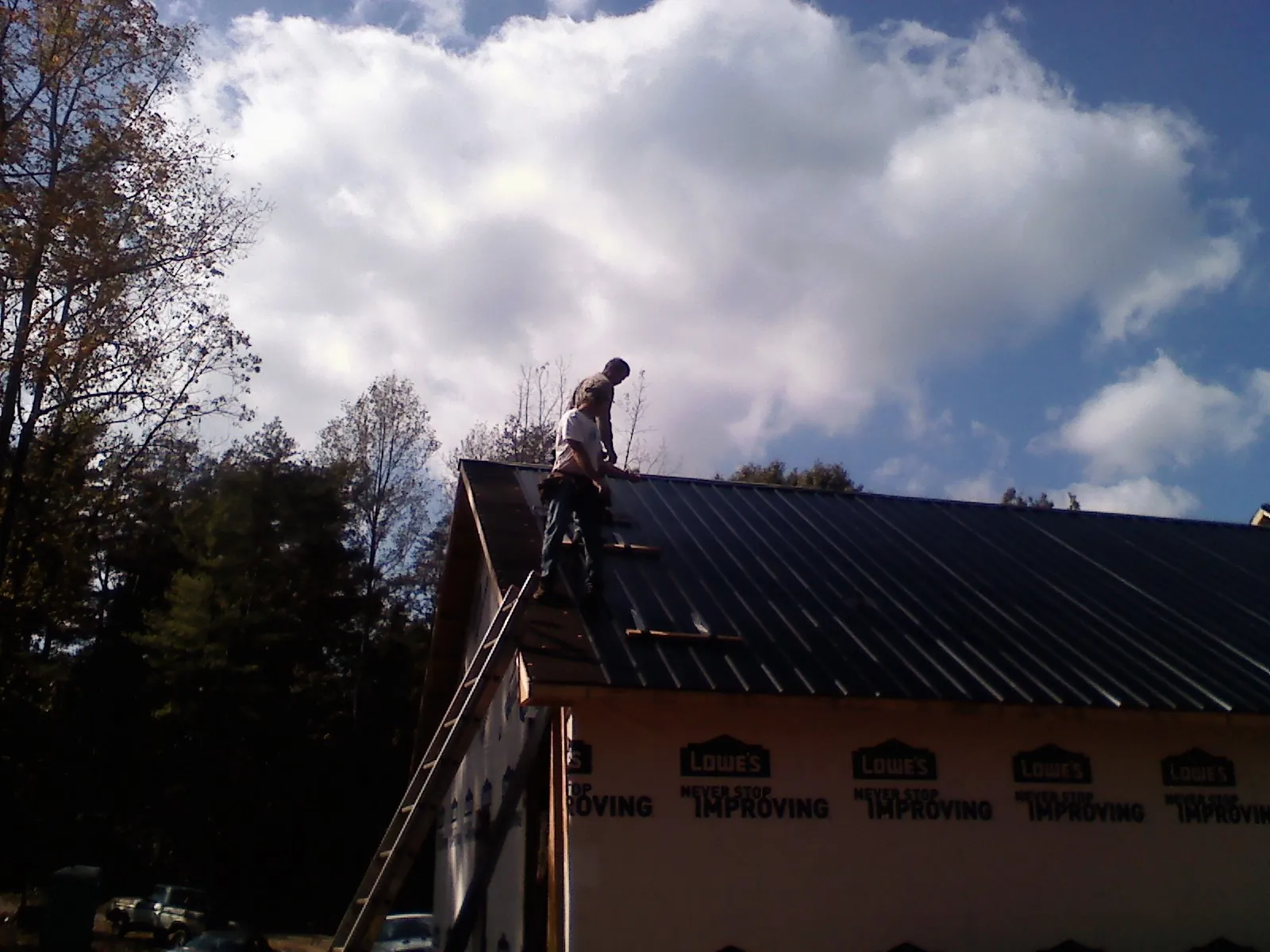 Roofer fastening dark metal panels high against a cloudy sky, from a Roof Inspection job in Wallsburg