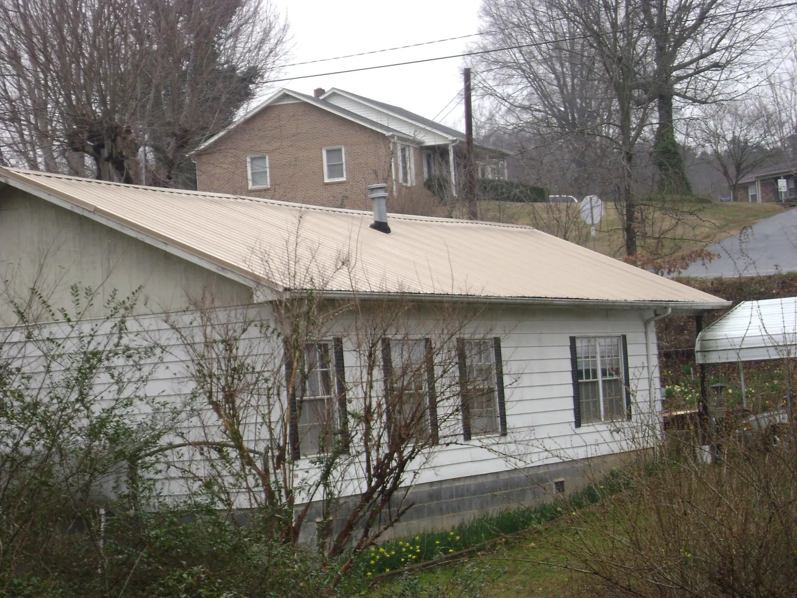 Tan metal roof on a white sided house set into a hillside — Commercial Roofing by Roofing Brothers in Wallsburg