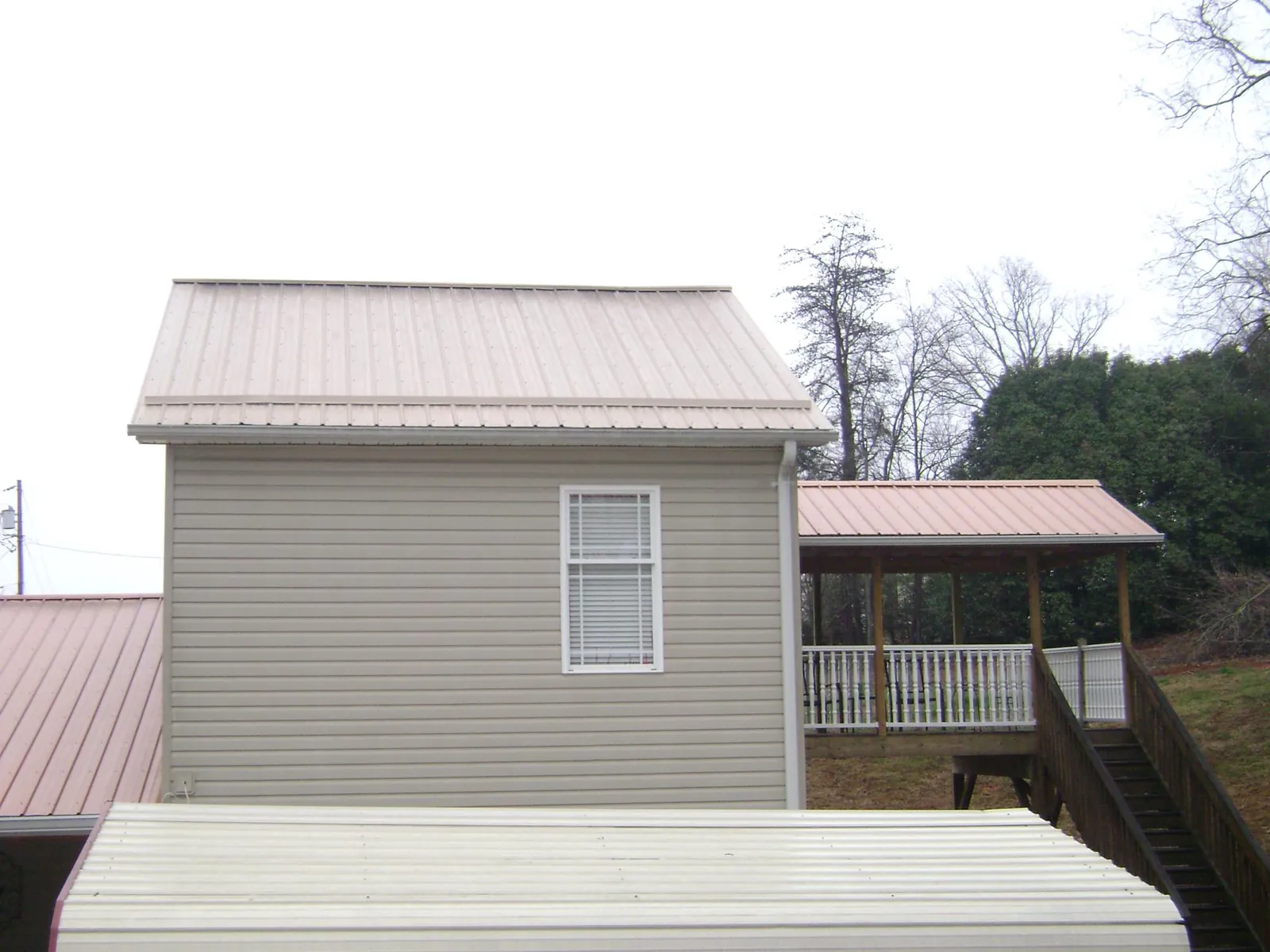 Tan metal roofs on a two story addition and attached porch, from a Roof Replacement job in Wallsburg